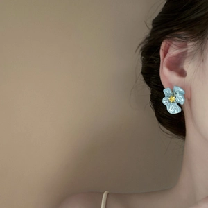 Gros plan d'une boucle d'oreille fleur bleue avec coeur jaune sur une oreille