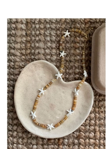 Detail shot of starfish beaded necklace with brown and white pearls on ceramic dish