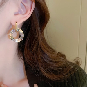 Close-up of golden geometric earrings with colorful mother of pearl and inlaid crystals