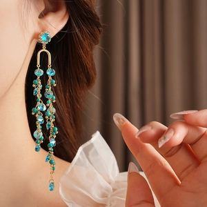 Macro detail of long tassel earrings with green crystals and gold chains on a model