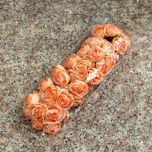 Detail of orange faux rose heads in a plastic bag on a granite surface for DIY crafts