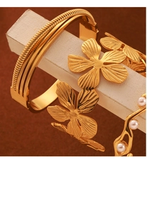 Close-up of 18K gold plated bracelets featuring textured metal floral and pearl accents