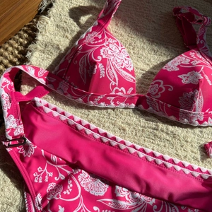 Bikini rosa a fiori con bordi a conchiglia bianchi su un asciugamano beige strutturato