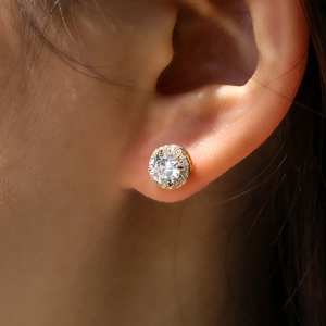 Macro shot of gold halo stud earrings with a large round central zircon on the ear