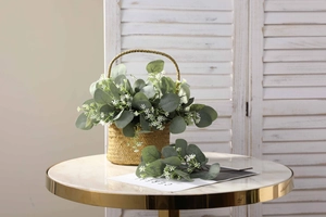 Artificial eucalyptus and gypsophila plants in a woven basket on marble table