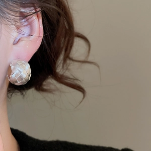 Detailed close-up of a silver spherical stud earring with woven texture on model