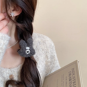 Detail view of a cute dark grey plush rabbit hair clip worn by a model in a cozy setting