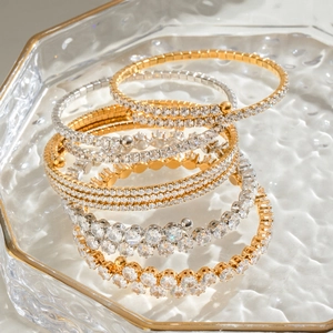 Luxurious gold and silver stainless steel bangles with clear zircon stones on a glass tray