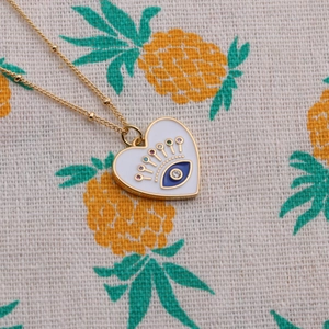 Gold-plated beaded necklace with heart enamel evil eye pendant on pineapple cloth background
