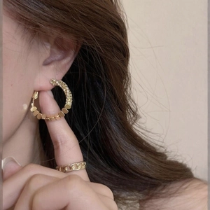 Detailed shot of large geometric gold hoop earring and Cuban chain ring on female model