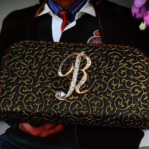 Elegant gold letter R brooch with sparkling crystals on a black clutch bag handle