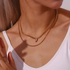 Detail of layered gold cuban chain and dainty necklace with teardrop zircon pendant
