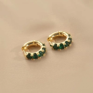 Close-up of gold hoop earrings set with green cubic zirconia on soft nude fabric