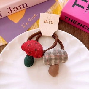 Close-up of two handmade cotton mushroom hair ties in red and plaid on a display card