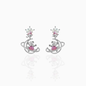 Dettaglio ravvicinato degli orecchini con orsetto e stella con perla rosa su sfondo bianco