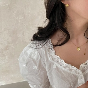 Close-up of gold shell earrings and sunburst pendant necklace on a female model