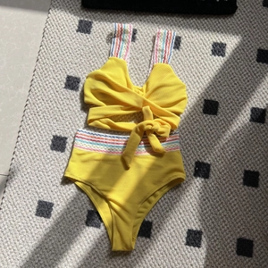 Flat lay of yellow seersucker bikini set featuring vibrant rainbow wave braided straps