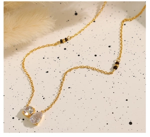 Detailed view of gold necklace with round and teardrop zircon pendants and black beads