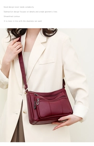 Detail of wine red crossbody bag with multiple zippers and pebble leather texture on model