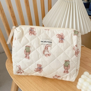 Quilted beige cosmetic bag with forest bear print on a wooden chair with cozy decor