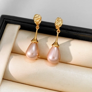 Detail of tear-drop pink pearl earrings with textured gold studs in a velvet jewelry box