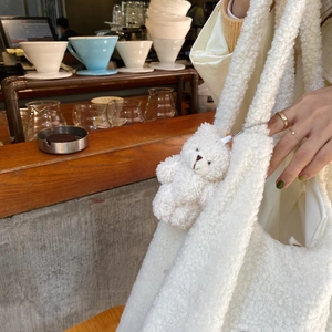 Detail of white faux shearling tote bag featuring a cute matching plush bear charm