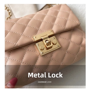 Close-up of golden rectangular hardware lock and diamond quilted stitching on beige bag