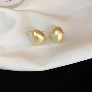 Matte gold brushed heart earrings on white silk background with elegant hook design