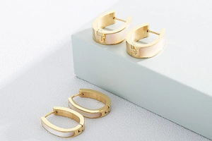 Detail of gold-plated U-shaped earrings with mother of pearl shell inlay on a grey stand