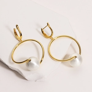 Macro view of gold-plated earrings with brushed texture pearls and metallic accents