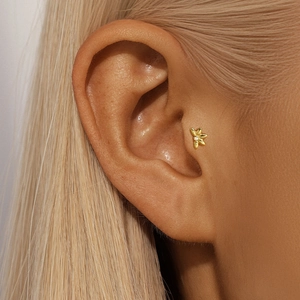 Close-up of a delicate gold flower cartilage stud earring with center crystal on ear tragus
