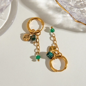 Detail of gold hoop earrings featuring green natural stones and tassel charms on white