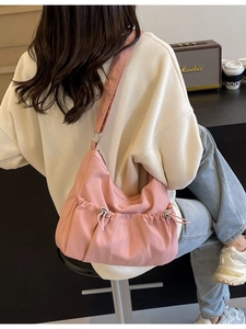 Pink nylon crossbody bag with pleated details shown on model in a cozy cafe setting