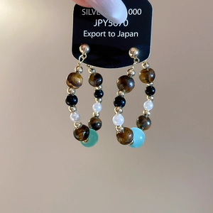 Detail of beaded hoop earrings featuring tiger eye, black, white, and sky blue beads