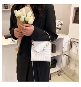 Detail of white quilted handbag with metallic ring handle and silver chain strap