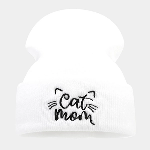 Close-up of Cat Mom embroidery and black cat whiskers on a white knitted beanie hat