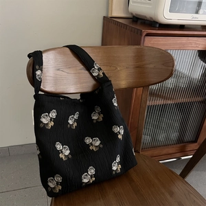 Floral jacquard tote bag with rose patterns on black textured fabric hanging on wooden chair