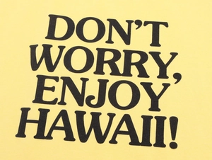 Detail of yellow knit fabric showing Don't Worry Enjoy Hawaii printed slogan