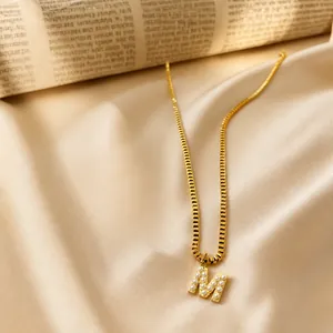Detail of a gold box chain necklace with a faux pearl-inlaid letter M pendant