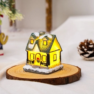 Close-up of glowing resin Christmas house ornament with snow details on wooden base