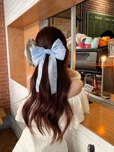 Detail of light blue mesh bow hair clip on long wavy hair in a cozy cafe setting