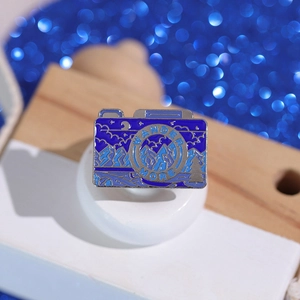 Macro shot of camera enamel pin featuring mountain scenery and Wander More text detail