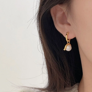 Close-up of a gold hoop earring with a white pearl drop worn on a model ear