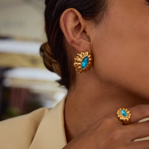 Detailed close-up of a gold-plated flower ring and stud earrings with blue gemstones