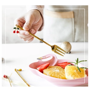Detail of a golden dessert fork featuring a cute cherry charm on a pink flamingo plate