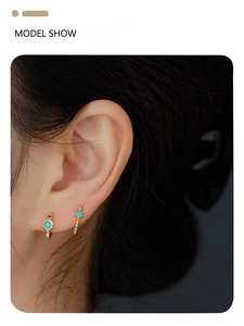 Close-up of model wearing gold huggie hoop earrings with small blue turquoise stones
