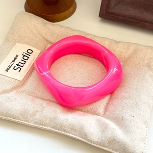Close-up of a glossy pink resin square bangle resting on a soft quilted cushion