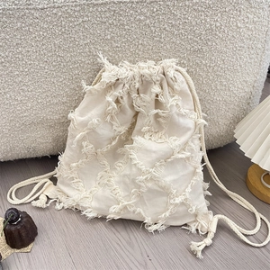 Detail of cream canvas backpack featuring fringe tassel and textured diamond pattern