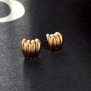 Detail shot of golden C-shaped earrings with vertical textured stripes and high gloss finish