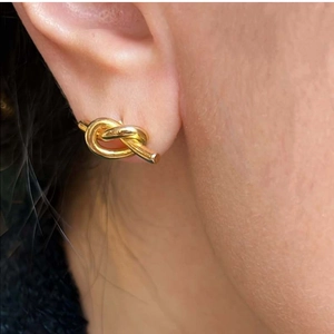 Close-up of minimalist gold knot stud earring worn on ear with polished metal finish